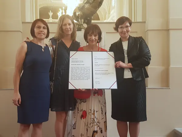 Štiri osebe stojijo skupaj v dvorani in v rokah držijo odprto listino državne nagrade.