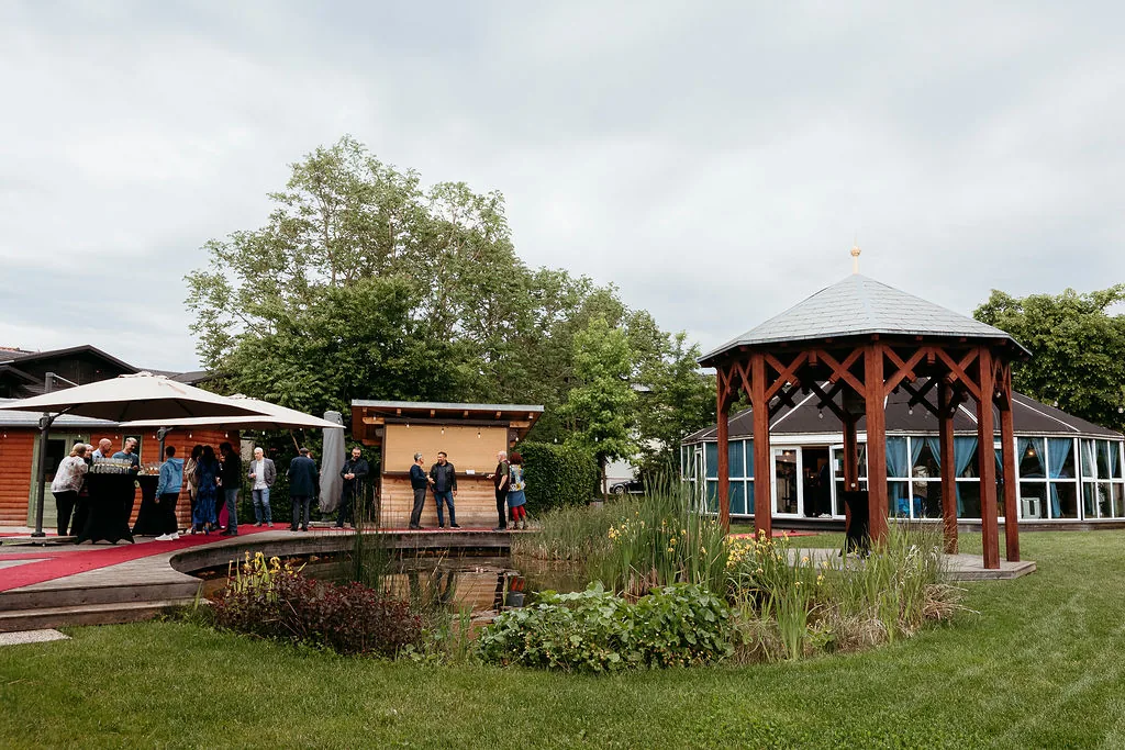 Vrt z ribnikom in paviljonom, v ozadju gostje na rdeči preprogi.
