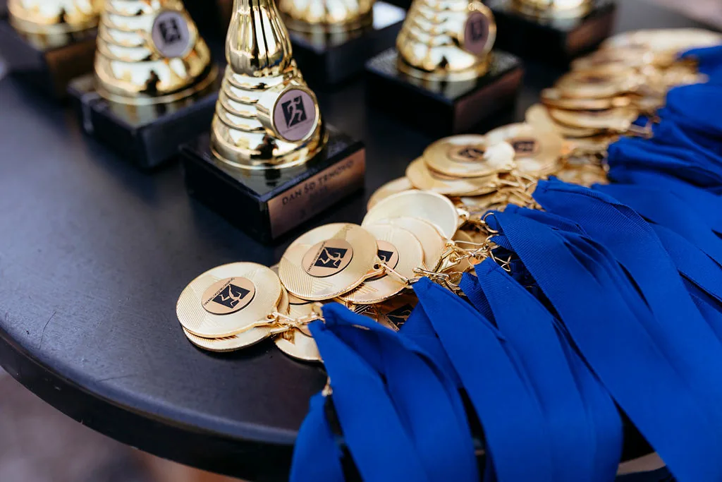 Pokali in medalje z modrimi trakovi na črni mizi.