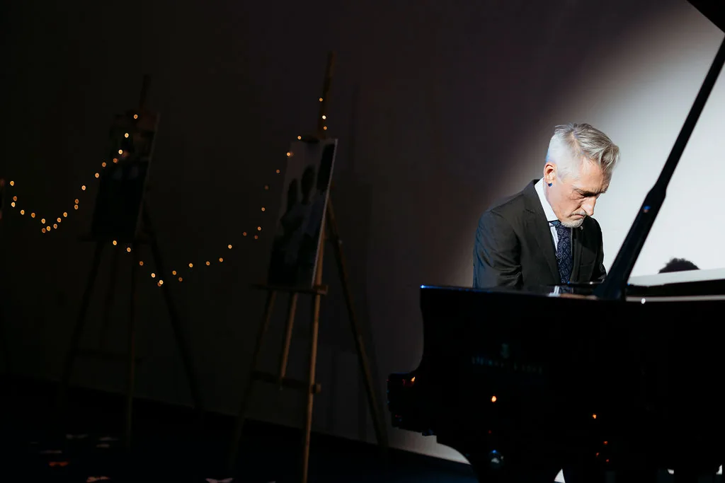 Pianist ob klavirju na temnem odru s svetlečimi lučkami.