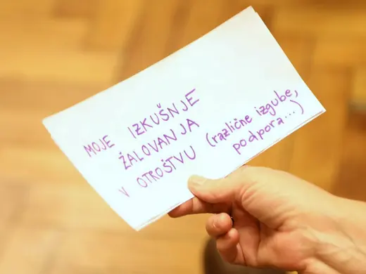 Roka drži list papirja z rokopisnim napisom o izkušnji žalovanja v otroštvu.